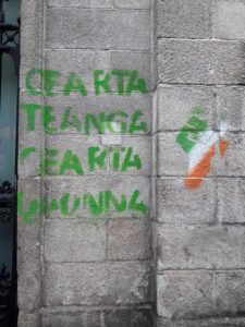Graffiti "Cearta Teaga, Cearta Daonna" = "Language RIghts, Human Rights" in green stencilled letters on a gray cinderblock wall with a fist in the green, white, and orange Irish tricolor